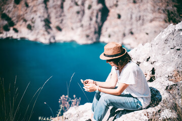 Traveler girl in a hat with a smartphone in her hands looks from a cliff at the Oludeniz Butterfly Valley, travel to Turkey.