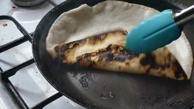 Traditional tasty Indian Partha preparation turning charred hot pancake cooking on stove in pan