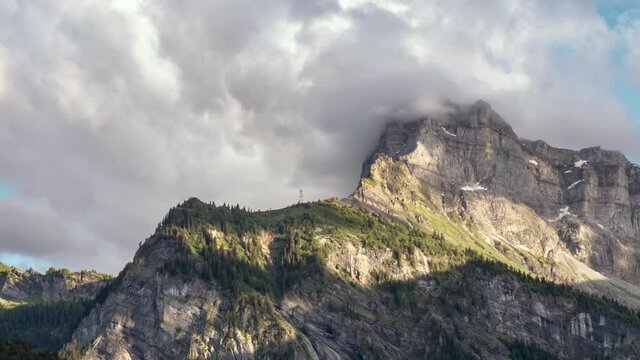 Time lapse, dramatic clouds collide against a rocky peak in Alps during sundown