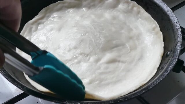 Preparing turning tasty Indian Partha hot pancake cooking on stove in pan dolly left