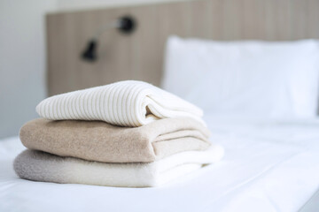 Stack of beige wool Sweaters on bed in luxury hotel or resort or home. Relax, autumn or winter clothes, laundry and vacation concepts