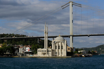 Fototapeta na wymiar The Ortakoy mosque, also known as Buyuk Mecidiye, is seen backgrounded by 15 July Martyrs bridge in a photo taken from a ferry boat in Bosporus strait, Istanbul, Turkey.