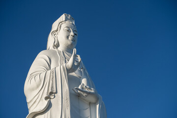 Fototapeta premium Detail of Lady Buddha statue in a Buddhist temple and blue sky background in Danang, Vietnam. Closeup, copy space