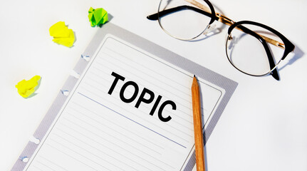 On a sheet from a notebook the inscription TOPIC, next to glasses and pencil.