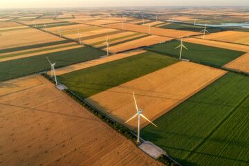 Aerial view of renewable windmills turbines supplying cultivation area with eco power getting energy from wind blowing on vast area of agriculture meadows next to sea. Alternative electricity