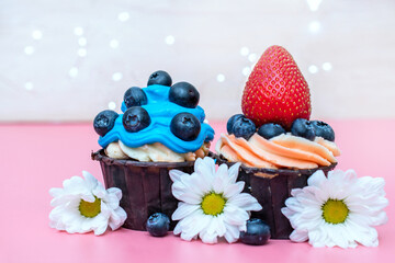 Obraz na płótnie Canvas two cupcakes decorated with blue cream with blueberries and beige cream with strawberries.