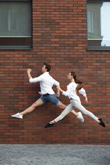 One way to go. Jumping young couple in front of city building wall, on the run in jump high....