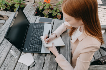 Digital nomad, freelancer, new normal work process. Young redhead Woman Working on Laptop in Street...