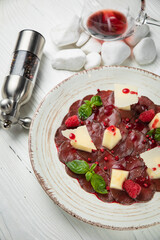 veal carpaccio with parmesan and pomegranate sauce. On a white wooden table.
