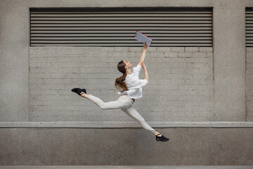 Paperwork. Jumping young woman in front of city building wall, on the run in jump high. Hurrying up...