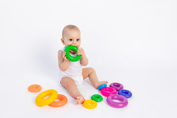 Fototapeta na wymiar cute boy 8 months old playing with a pyramid on a white isolated background and licking toys, place for text, early development of children