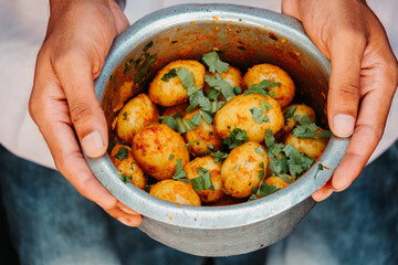 Closeup shot of hand holding dum aloo in bowl