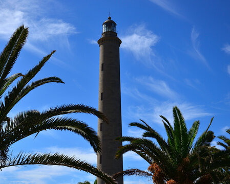 Imposing stone lighthouse among palm trees and blue sky, Maspalomas, Gran Canaria, Spain