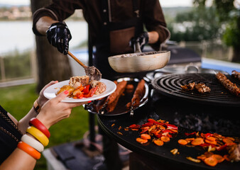 The chef serves food - meat and vegetables in a plate to the guest. Barbecue in the garden