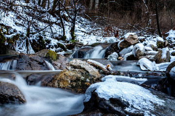 semi frozen small waterfall in a stream in the mountains in deep winter with ice