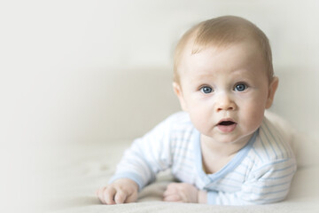 Cute six month old baby lying on his stomach on a bed on a beige background. Soft focus, copy space.