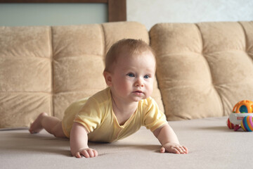 Fototapeta premium Baby lying on his stomach on a bed on a beige background. Soft focus, copy space.