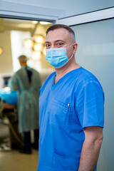 Professional surgeon. Serious man wearing medical uniform and mask standing in the operation room. Working in the hospital