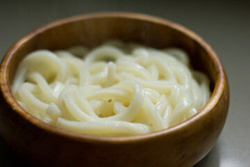 Steaming bowl of Japanese udon noodles in a round wooden bowl.