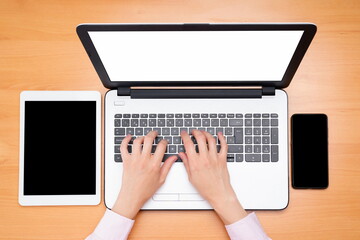 Woman hands typing on the computer on a brown table, mobile phone and tablet on the table