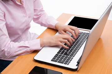 Woman hands typing on the computer on a brown table, mobile phone and tablet on the table