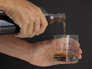 Close-up. Male Pouring Dominican rum from bottle into glass.