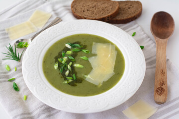 Soup of leeks, scallions green spring onions and potatoes garnished with pesto, scallions and shaved parmesan. In the background is black rye bread, wooden spoon and shaved parmesan
