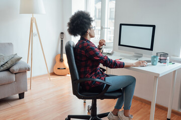 Comfortable workplace. Side view of afro american woman looking at computer screen while working or learning online from home
