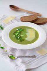 Soup of leeks, scallions green spring onions and potatoes garnished with pesto, scallions and shaved parmesan. In the background is black rye bread, wooden spoon and shaved parmesan