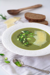 Soup of leeks, scallions green spring onions and potatoes garnished with pesto, scallions and shaved parmesan. In the background is black rye bread, wooden spoon and shaved parmesan