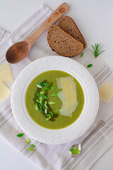 Soup of leeks, scallions green spring onions and potatoes garnished with pesto, scallions and shaved parmesan. In the background is black rye bread, wooden spoon and shaved parmesan