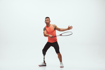 Athlete with disabilities or amputee isolated on white studio background. Professional male tennis player with leg prosthesis training in studio. Disabled sport and healthy lifestyle concept.