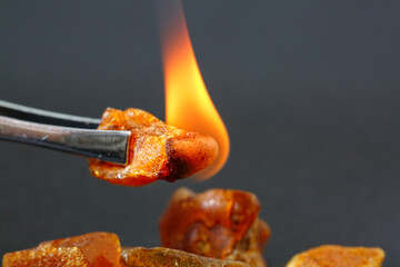 Physical properties of amber. Properties of the sun stone. Burning piece of amber on a gray...