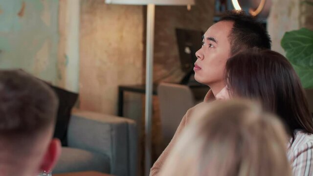 Young serious stressed 20s Asian manager businessman is anxious and bored, tired of sitting at busy office team meeting.