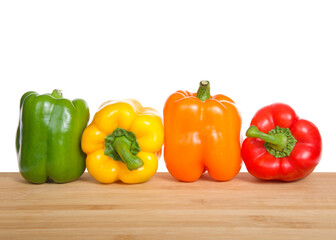 Close up of bell peppers on a dark wood table lined up in a row. Green, yellow, orange and red.