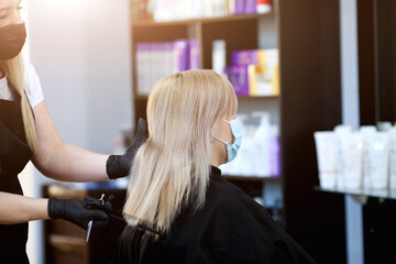 Hairdresser in rubber gloves and a medical mask combing the hair of a client.