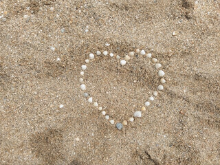 A large heart of seashells laid out on sea sand. Photograph, top view.