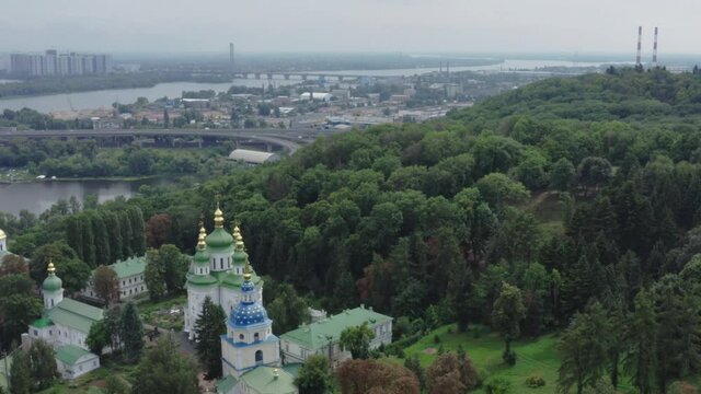 Quadrocopter flight over Vydubychi monastery with copper green roof, church bell towers and gold domes. Vydubychi Monastery with its main temple, refectory and bell tower among the trees