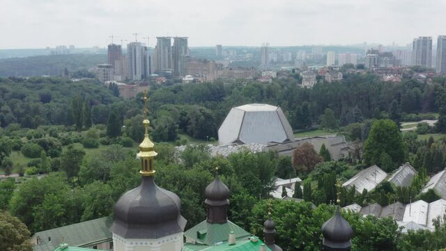 Quadrocopter flight over Vydubychi monastery with copper green roof, church bell towers and gold domes. Vydubychi Monastery with its main temple, refectory and bell tower among the trees