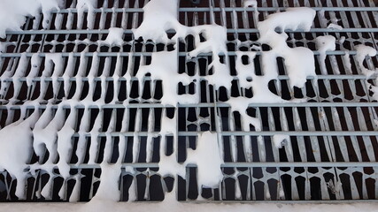 Close-up of white pieces of snow on a metal grate. Snow falls through the grating, revealing voids. Abstraction of snow and metal lattice. On a winter day, outdoors in the evening. Texture.