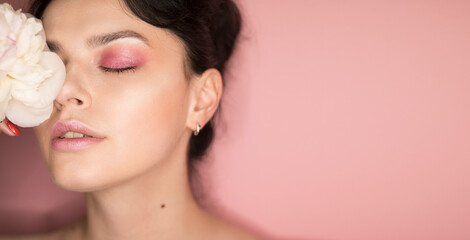 Naklejka premium Girl with pink makeup with a peony in her hands on a pink background 