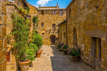 Flowers fill a honey stone courtyard in the hill top settlement of Civita di Bagnoregio in Lazio, Italy in summer