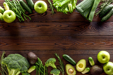 Green vegetables background. Сucumber, avocado, broccoli, beans, leek and fresh apple on dark wooden background top view mockup