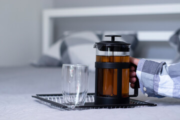 french press tea and a glass with a double bottom on a handmade black metal tray in bedroom on a bed. home interior and decor concept. High quality photo