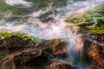 Fototapeta na wymiar water splash on rocks sunset over the sea