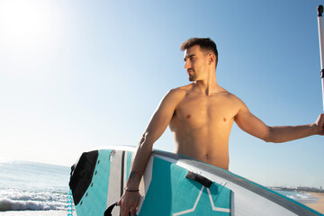 Fototapeta premium Attractive and athlete man with a paddle surfboard on the beach