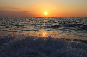 Scenic view of the sea sunset, orange sky, sun on the horizon, splashing waves and sea foam in the...