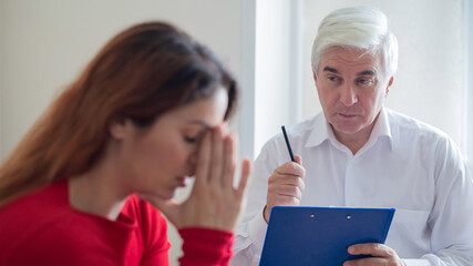 A frustrated crying woman holds palms in her face at a session with a male psychologist. Mature gray-haired psychotherapist talking to a female patient with depression and neurosis. Unbalanced psyche.