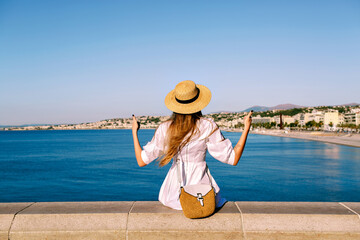 Stylish woman posing back in front of amazing view on Nice French Riviera sea and city, showing good gesture, summer traveling time.
