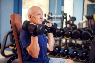 Fototapeta na wymiar A portrait of senior man in the gym training with dumbbells. People, health and lifestyle concept